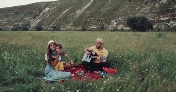 Beautiful picnic time with a young family, man playing at the guitar — стоковое видео