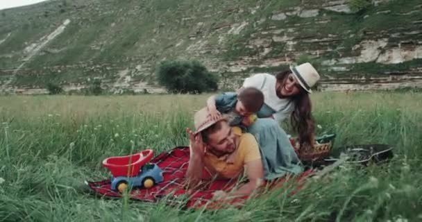 Mama en papa spelen met de kinderen van een baby op de picknick, in het midden van de landschap — Stockvideo