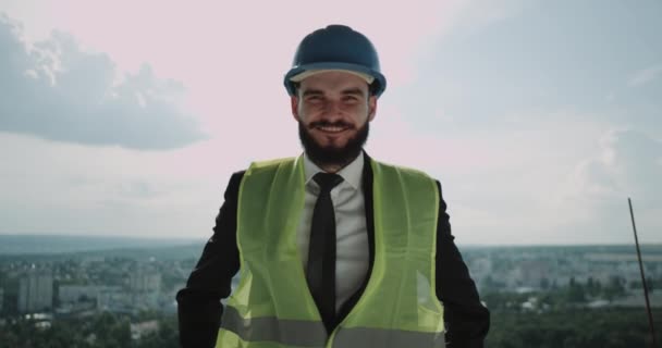 Jonge architect op de bouwplaats op de top, close-up glimlachend op zoek naar de camera — Stockvideo