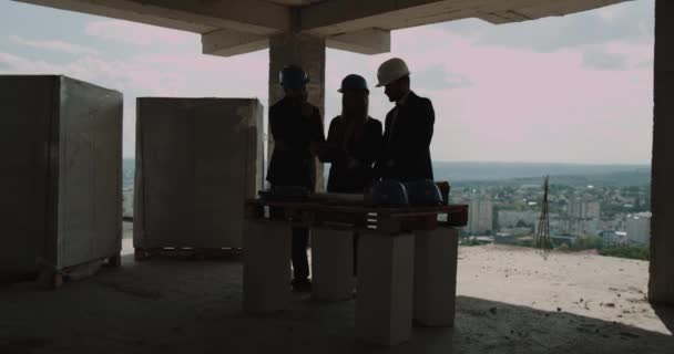 Инженеры или архитекторы обсуждают на строительной площадке план строительства. contre jour — стоковое видео