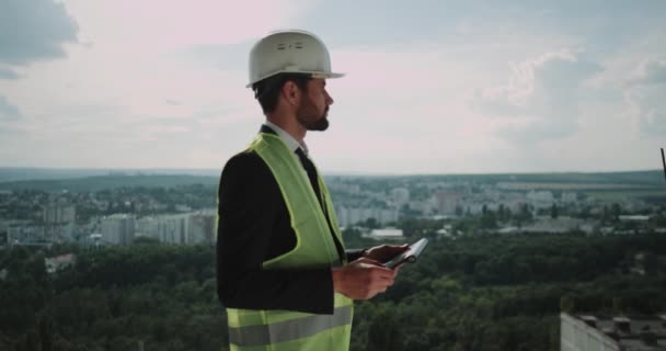 Volwassen ingenieur maakt gebruik van de tablet in werking controles de tekening van gebouw. — Stockvideo