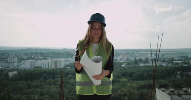 Expertin Ingenieurin auf der Oberseite des Gebäudes blickt lächelnd in die Kamera und dreht sich um mit dem Rücken zum erstaunlichen Blick auf die Gebäude. — Stockvideo