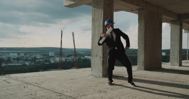 Danse beau jeune ingénieur sur le toit du bâtiment dans la construction — Video