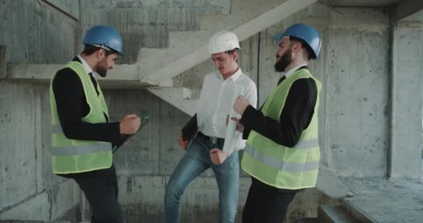 Tres arquitectos bailando en la obra al final de la jornada laboral, llevando chalecos de alta visibilidad y sombreros duros . — Vídeo de stock