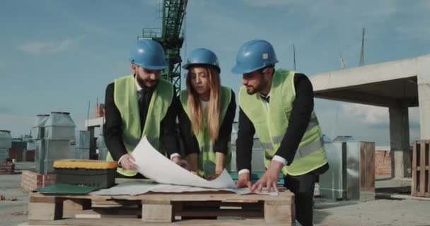 Unga ingenjörer team talar och tittar på byggplanerna i byggarbetsplatsen. 4, k — Stockvideo