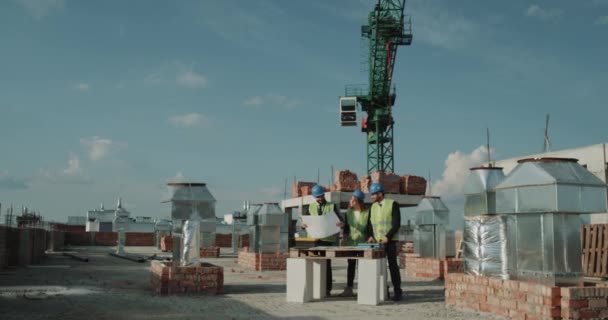Tres trabajadores del sitio de construcción analizando el trabajo mirando a su alrededor a la construcción, manchan en medio del sitio de construcción — Vídeos de Stock