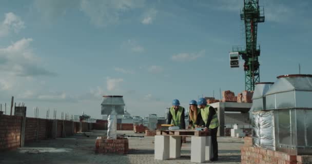Молоді інженери обговорюють карту плану будівництва, на будівельному майданчику — стокове відео
