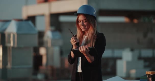年轻漂亮的女性在建筑工地上用无线电说话, 分析施工计划, 最后快乐跳跃. — 图库视频影像