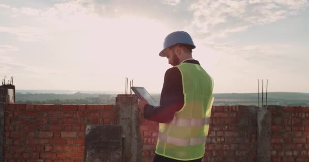 Närbild ung ingenjör på taket husbyggande analysera projektet att bygga på en surfplatta och tala med en radio. 4k — Stockvideo