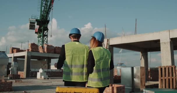 Cantiere con gru di fondo, due ingegneri esperti che camminano e discutono dei nuovi appartamenti . — Video Stock