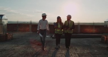 İnşaat alanında yeni bir daire çatıda yürürken üç işçilerden şaşırtıcı günbatımı arka plan üzerinde tartışma, var. Yavaş hareketleri. 4k