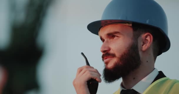 Крупним планом розмовляючий бізнесмен використовує радіо і носить шолом безпеки . — стокове відео
