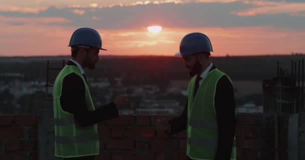 Dva zaměstnance ze staveniště hrát s rukama na střeše budovy. — Stock video