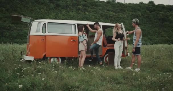 Two couple have fun and dancing in the middle of landscape at picnic time, hip friends and retro bus. 4k — стоковое видео