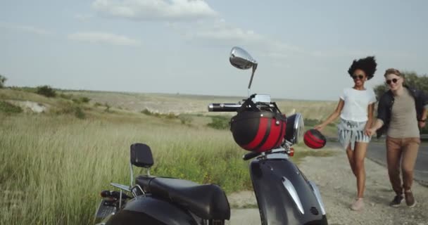 Couple holding hands running towards retro motorbike in the green desert landscape. 4k — Stock Video