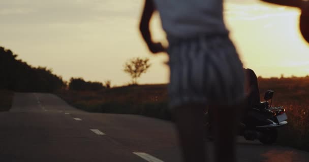 Csak csodálatos égen fények, fiatal férfi az út közepén áll a retro motorkerékpár és várakozás-re a fiatal nő, aki fut őt tartja a sisak. — Stock videók