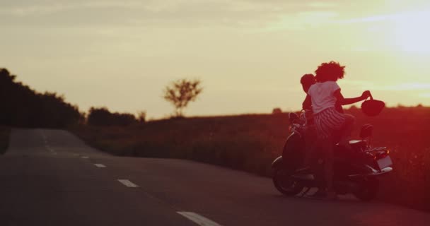 Jeune femme et les hommes, préparez-vous pour une balade sur leur moto rétro, ils se préparent à aller porter leur casque, vue imprenable sur la lumière du soleil. 4k — Video