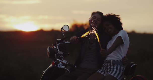 Krásná mladá žena a muž stojí na jejich retro motocykl drží světluškami a užívat si čas při západu slunce. — Stock video