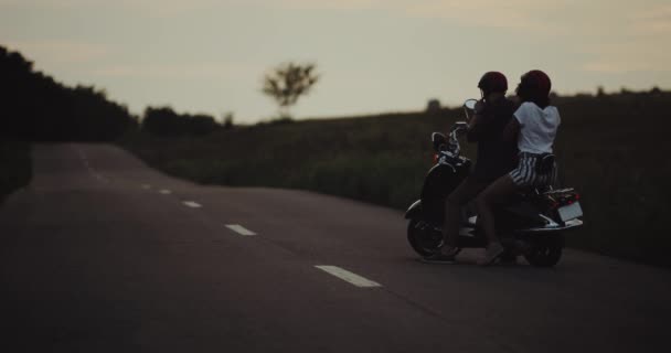 Couple se préparer pour une balade sur leur moto rétro dans la soirée, portant le casque, puis aller sur la route sans voitures . — Video