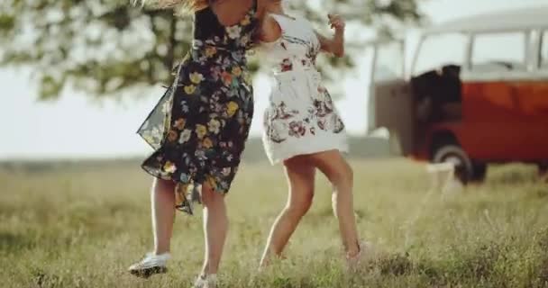 Дві молоді жінки танцюють посеред природи в ретро-сукні, на фоні красивого ретро автобуса — стокове відео