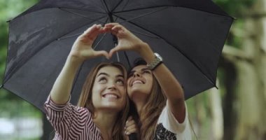 İki güzel iyi görünümlü bayanlar closeup elinden bir kalp yapma şemsiyesi altında.