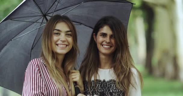 Потрясающие молодые женщины улыбаются, глядя в камеру, под зонтиком. 4k — стоковое видео