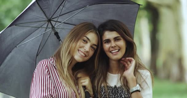 Funny emotion of two young female under the umbrella looking straight to the camera , large smile. — Stock Video