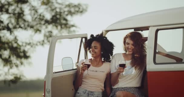 Two young woman picnic time , drinking wine and standing beside the retro bus , curly hair , good mood. — Stock Video