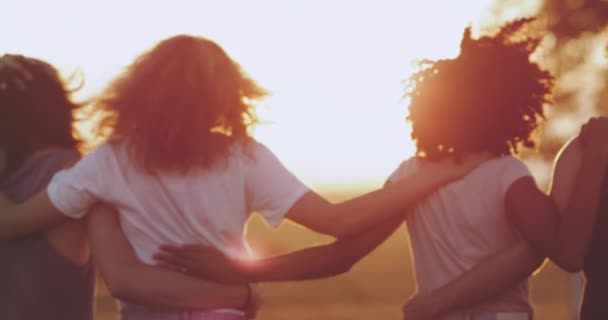 Une femme africaine aux cheveux bouclés avec ses amis marchant vers le champ, des lumières du ciel étonnantes, se tenant l'un l'autre. au ralenti — Video