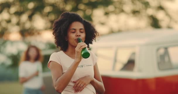 Улыбающаяся счастливая кудрявая африканская юная леди пьет пиво перед камерой на пикнике — стоковое видео