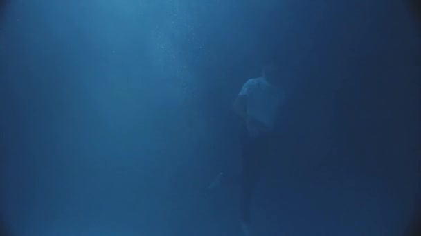 In de nachttijd onder water valt een man zwemmen dragen van de kleding, sommige maanlicht in het water. — Stockvideo