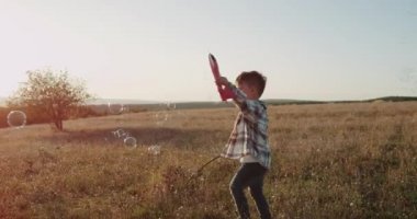 Küçük sevimli çocuk kırmızı bir uçak ile oynarken, rüya, günbatımı, şaşırtıcı tarlanın ortasında uçan etrafında bubbles. 4k