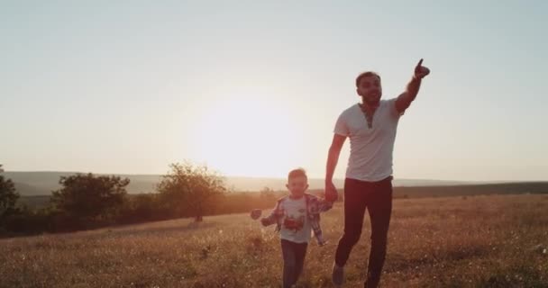 Pappa med sin son som kör på naturen, ser några måltider bort, bakgrunden fantastiska solnedgången. — Stockvideo