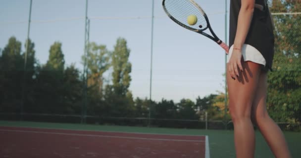 Tiempo de tenis en la noche, piernas musculares de mujer de primer plano, vence a la pelota de tenis con raqueta en la cancha de tenis . — Vídeo de stock