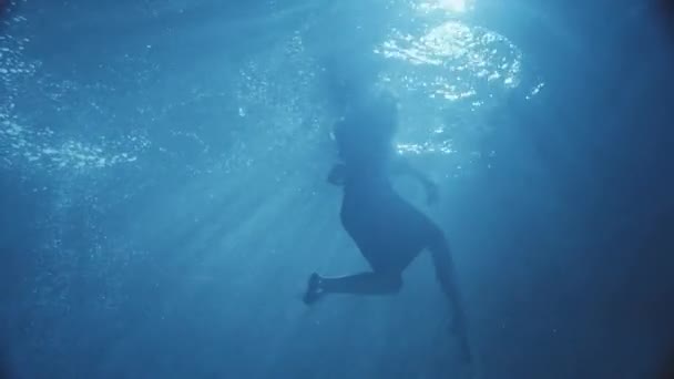 Een vrouw die het dragen van een jurk die zwemmen in een donkere pool, camera onder het water, geweldige bekijken. — Stockvideo