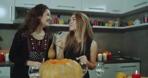 Sie spielen zwei Damen, die bei einer Halloween-Party zu Hause vor der Kamera stehen und etwas in der Hand halten, sie lächeln. — Stockvideo