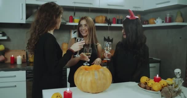 Tres chicas enmascaradas en la fiesta de Halloween bebiendo vino y tienen una gran conversación, todo alrededor está decorado para la noche de Halloween . — Vídeos de Stock