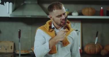 Genç adam onun mutfak bir bıçak ile oyun hazırlamak Cadılar Bayramı için sevme bıçak ve karizmatik kamera önünde gülümseyen. 4k