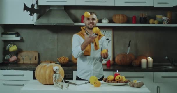 Χαρισματικός άνθρωπος ζογκλέρ με κάποια πορτοκάλια στην κουζίνα του, στο τραπέζι του, μπροστά από την κάμερα χαμογελώντας. — Αρχείο Βίντεο