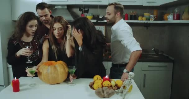 Festa em casa na noite de Halloween, jovens senhoras e senhores para cortar uma abóbora, tirando algo de uma grande abóbora, rosto curioso . — Vídeo de Stock