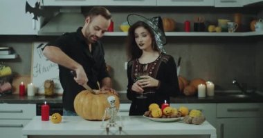 Cadılar Bayramı partisinde bir cadı onu arkadaş genç adam ile mutfak at için büyük bir Cadılar Bayramı Balkabağı, süslemeleri Cadılar Bayramı partisi için arka plan üzerinde Bayan kesmeye çalışırken sakallı maskeli güzel bir bayan