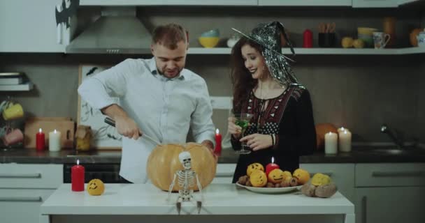 Una pareja se prepara para la fiesta de Halloween en su cocina, están decorando la mesa de la cocina, empezando a cortar una calabaza muy grande, la joven está enmascarada para Halloween. 4k — Vídeo de stock