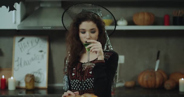 Detailní záběr na Halloween party Krásná Asiatka v čarodějnice pít zelený koktejl ze skla, Halloween atmosféru v kuchyni, velké dýně. — Stock video