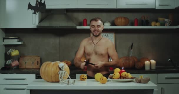 Spiel mit dem Messer ein Mann in seiner Küche, Vorbereitungen für Halloween-Party, er hat nackten Körper, schöne Atmosphäre auf dem Hintergrund. 4k — Stockvideo
