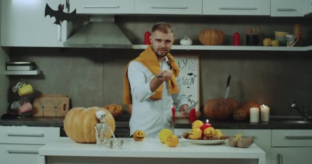 Homem carismático se preparar para a festa de Halloween em casa na cozinha jogando artístico com duas faca, decorações incríveis no fundo . — Vídeo de Stock