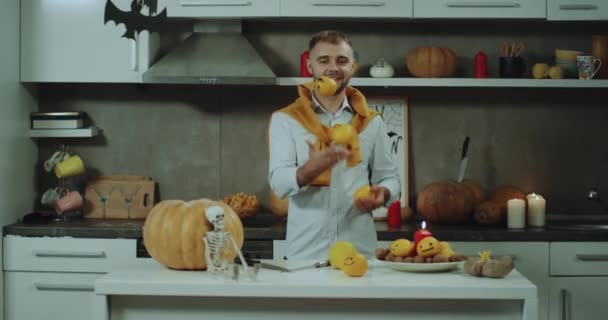 Jongleren man met sinaasappelen befor een Halloween-feest op zijn keuken voor de camera. — Stockvideo