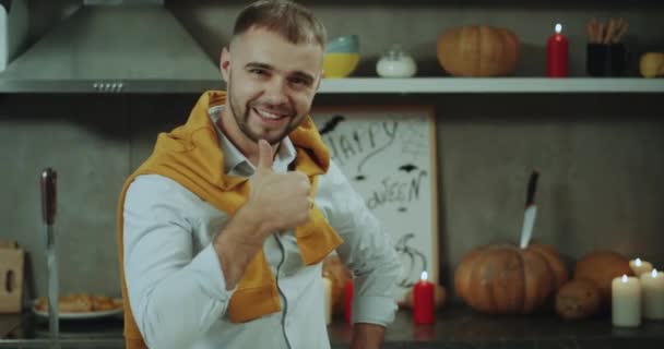 Крупним планом чоловік перед вечіркою на Хелловін, посміхаючись перед камерою, він встає за своїм кухонним столом, фоном дивовижні прикраси на Хелловін . — стокове відео