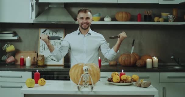 Hermoso hombre en la mesa de la cocina se preparan para cortar una gran calabaza de Halloween, con un cuchillo grande, hermosas decoraciones para Halloween . — Vídeos de Stock