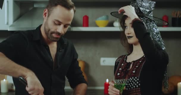 Харизматичный мужчина и женщина на Хэллоуинской вечеринке отлично проводят время вместе, улыбаясь, она пьет коктейль, а мужчина пытается что-то вырезать . — стоковое видео