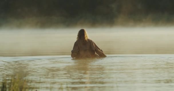 Ragazza dai capelli lunghi passeggia lungo un lago di colore blu intenso mentre il sole tramonta. 4k — Video Stock